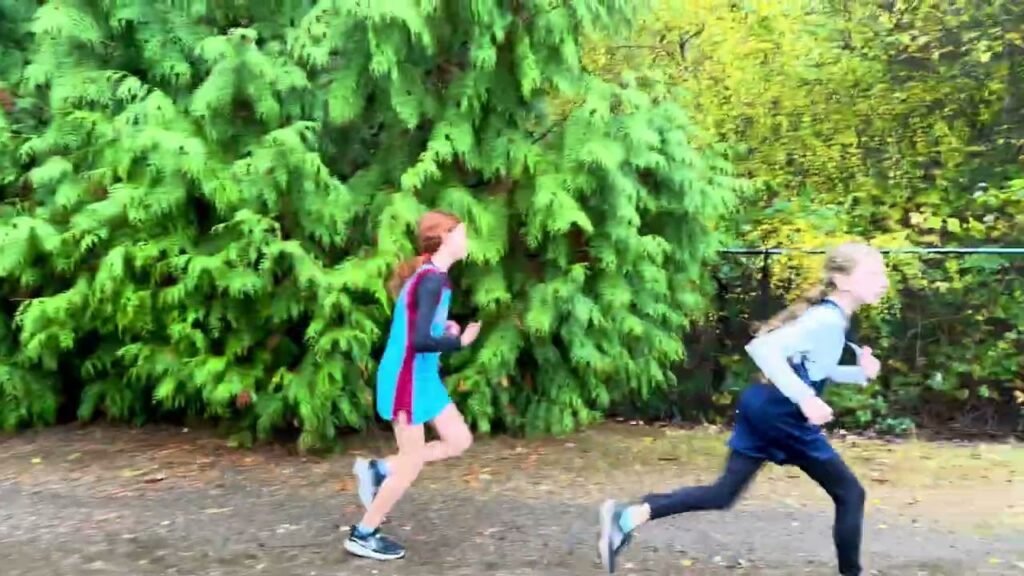 Two individuals running along a path bordered by a large green hedge. The image captures motion and energy in a natural setting.