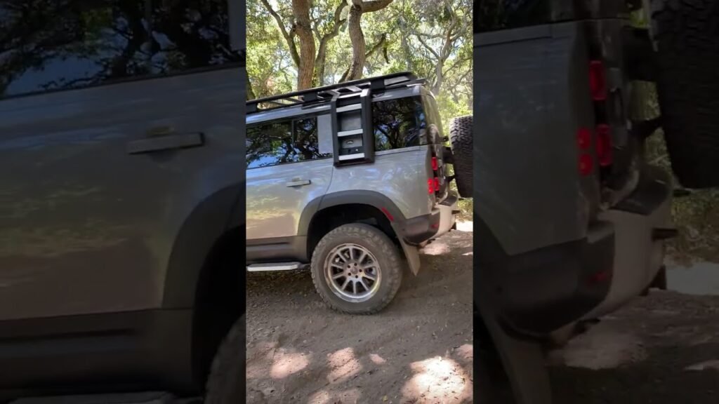 A silver off-road truck equipped with a roof rack and spare tire, parked in a shaded outdoor setting.