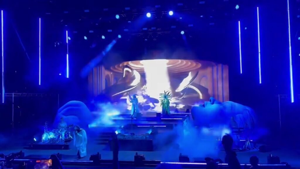A captivating stage performance bathed in vibrant blue lights with misty effects and a glowing backdrop.