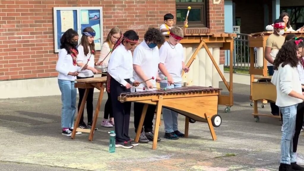 A group of students conducting experiments at wooden tables outdoors, wearing masks and casual attire.