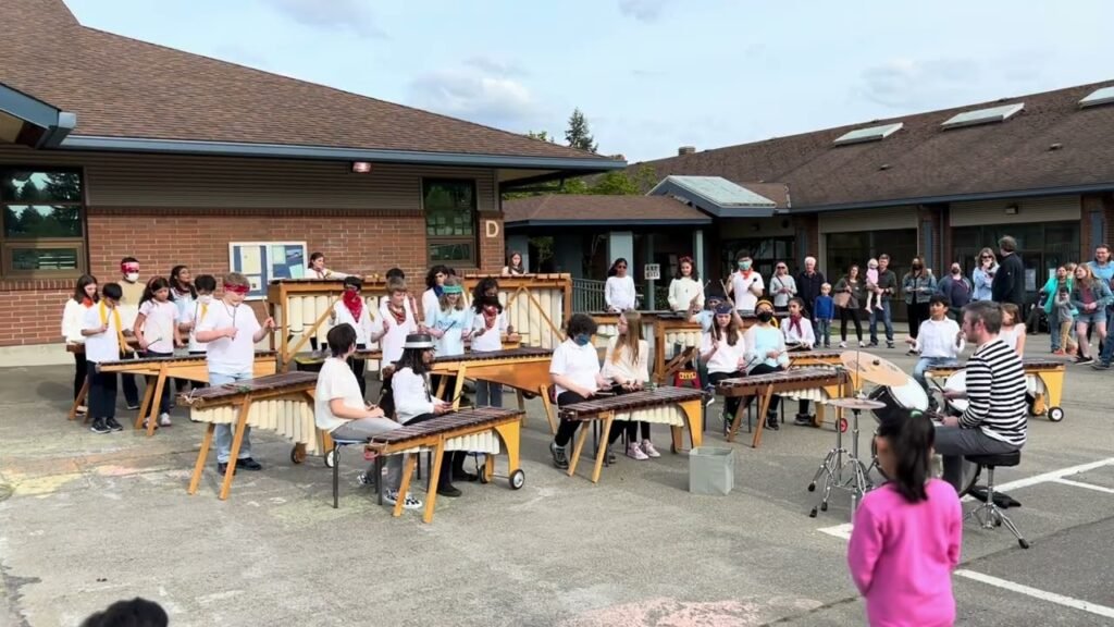 Children seated at wooden desks outdoors during a school activity on a clear day.
