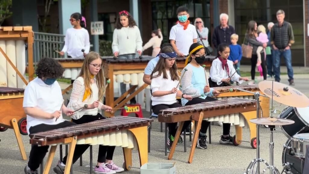 Young musicians playing hand percussion while singing and drumming under clear skies.