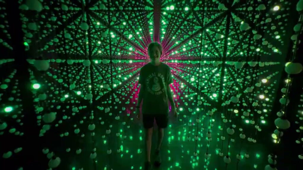 A person is surrounded by a canopy of green and pink lights forming a spiral pattern.