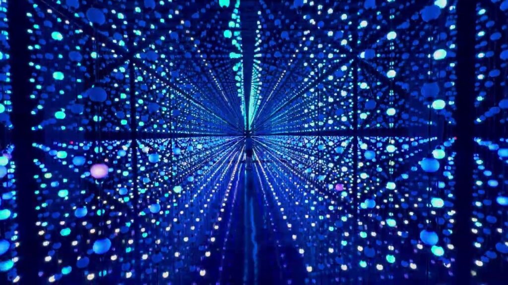 A view down the Eaton Runoff Tunnel filled with blue star-like light projections. The dark truss ceiling contrasts with the bright, immersive digital art display.