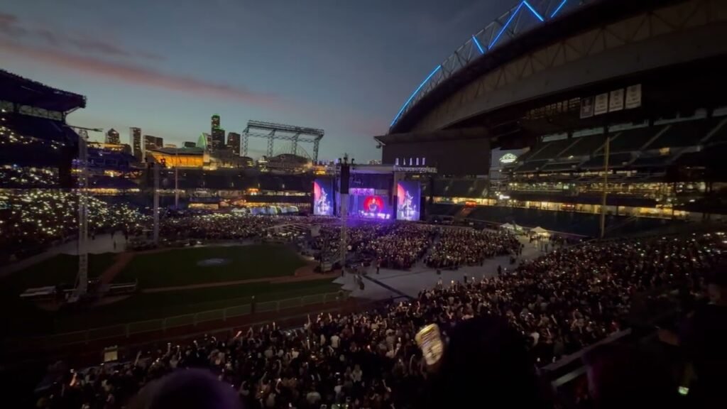 A wide-angle view of T-Mobile Park in Seattle, showing a concert stage with a large crowd and the downtown skyline at dusk.
