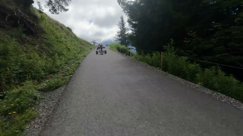 A paved path winds through a lush Pacific Northwest forest. Riders in the distance add sense of scale and activity.