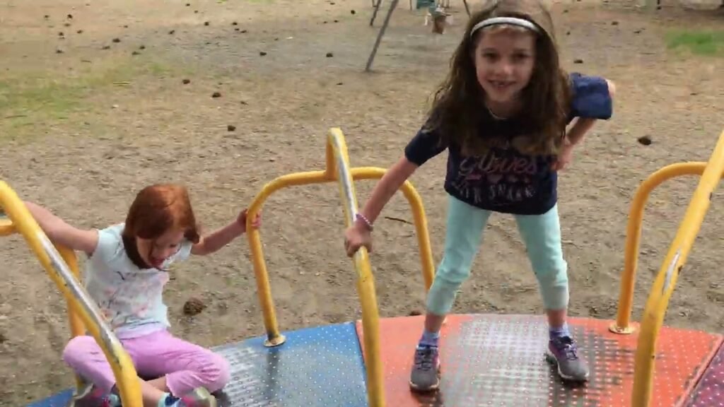 Children playing on a colorful playground spinner in a sandy area.