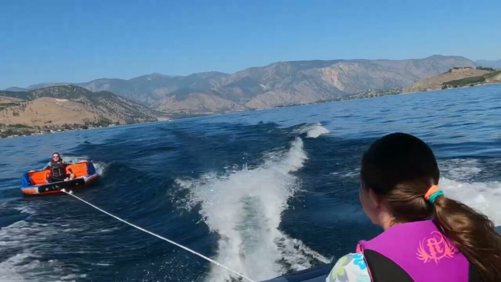 A person in a life vest water skiing as we cruise the lake, with mountains in the background.