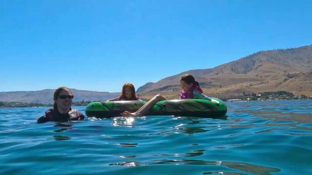 Enjoying a sunny day on a green lake inflant float. Family relaxing in a turquoise lake with mountains on a clear day.