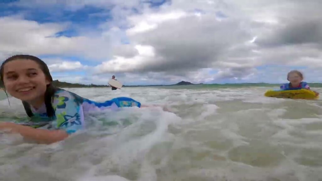 A young person and an older person enjoy the water in a tropical ocean setting under a cloudy sky.
