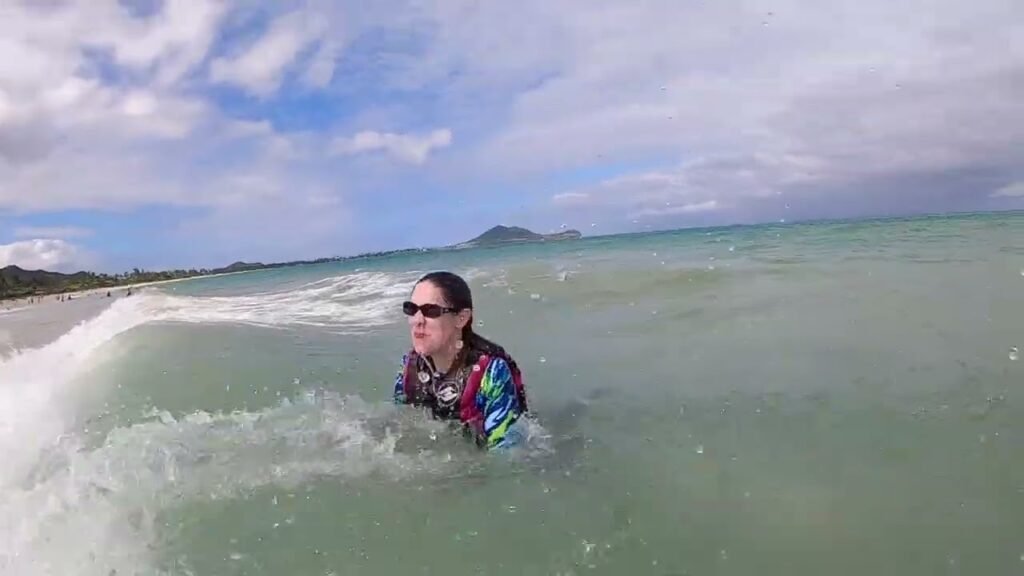 A person in a colorful rash guard enjoys the foamy waves at a tropical beach under a partly cloudy sky, captured in a series of action shots.