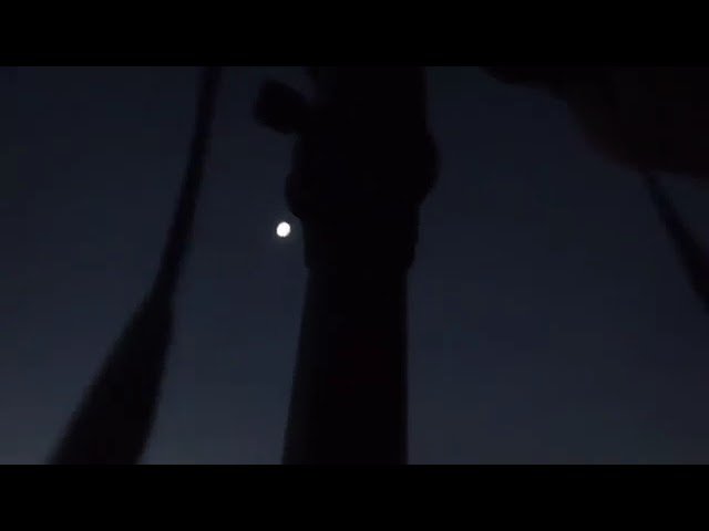 A hand silhouetted against the dark twilight sky with a bright moon and sailboat rigging. Captured from a Pacific Northwest sailing adventure blog.