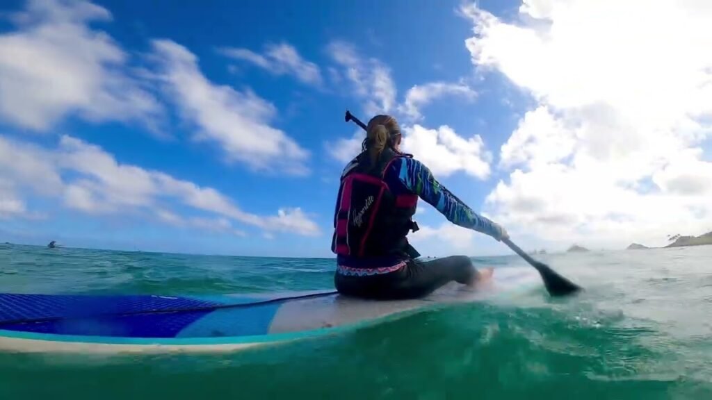 A person is paddleboarding on turquoise ocean water under a blue sky with clouds.