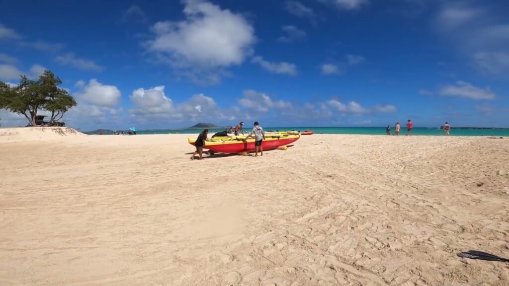 A vibrant red kayak rests on a pristine white sand beach under a bright blue sky with scattered clouds. Turquoise water stretches out in the distance, suggesting a tropical travel destination ideal for kayaking and beach relaxation.