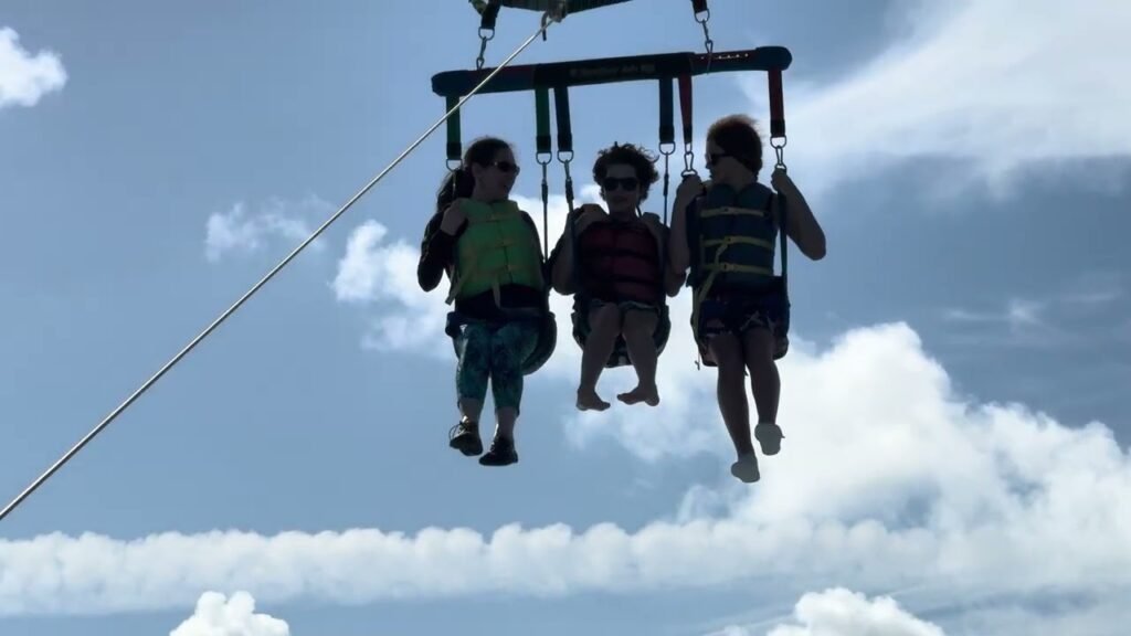 Three people riding on a zipline high in the sky with clouds in the background