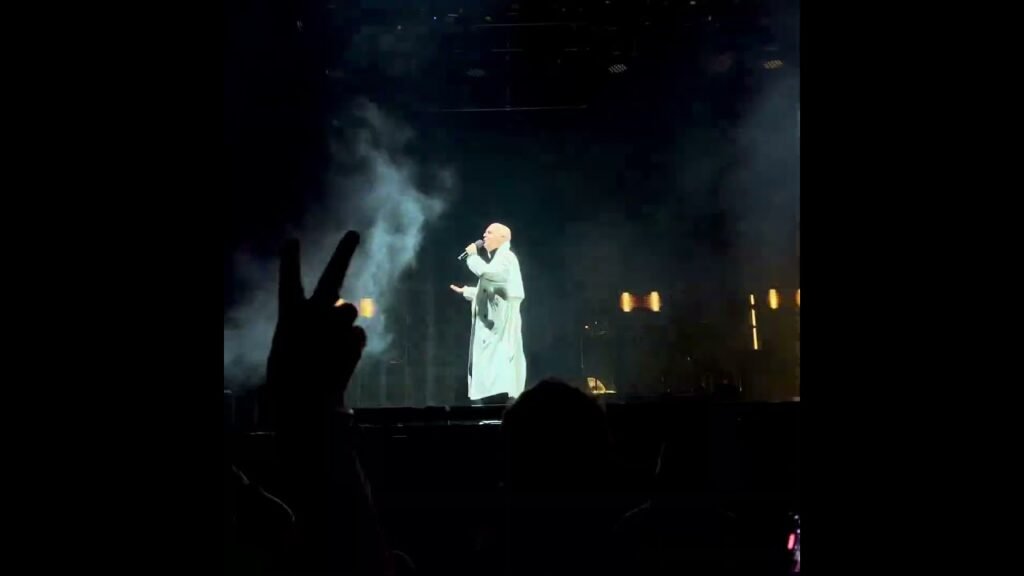 An atmospheric concert scene featuring a performer on stage and audience members at live event.