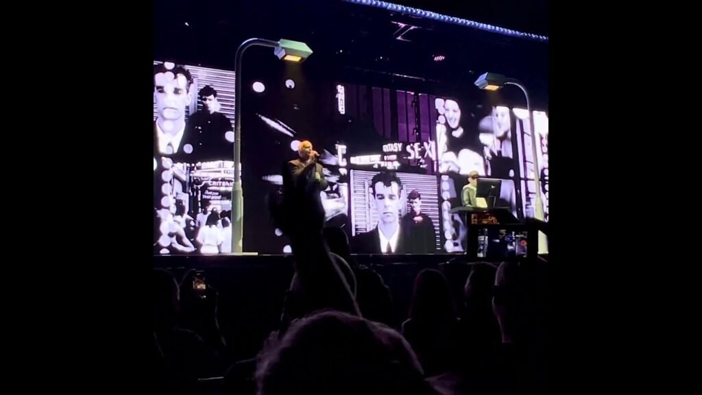 Vivid stage lights illuminating a performer and video screens at a live concert.