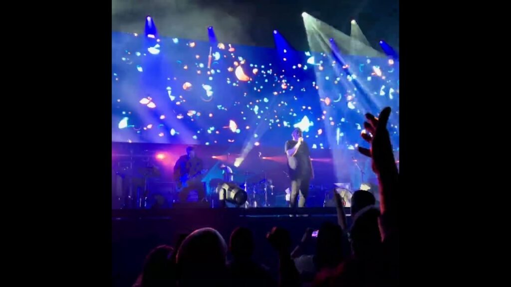A concert scene filled with vibrant blue stage lights and an active audience, capturing live music energy from the Pacific Northwest.
