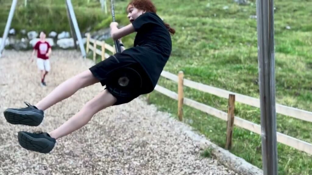 A child swings high above wood chips on a sunny day at a park.