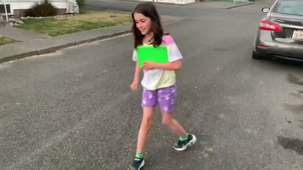 A person walking on a residential street collecting Easter eggs in a green basket.