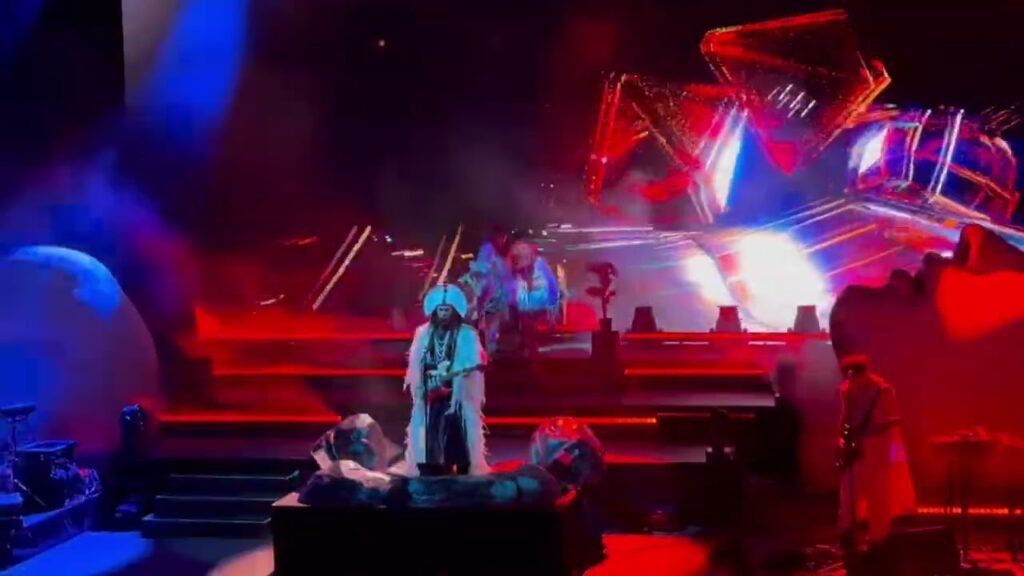 A rock band performs on stage under vibrant red and blue lights during a nighttime concert.