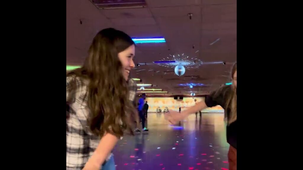 A person smiling and extending a hand at an indoor ice rink with colorful lights. The setting highlights a fun and social atmosphere.