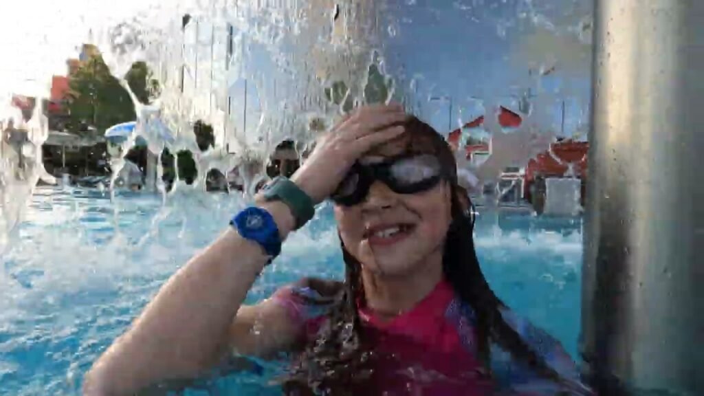 A swimmer with goggles shielding eyes from a fountain spray, wearing a blue wristband.