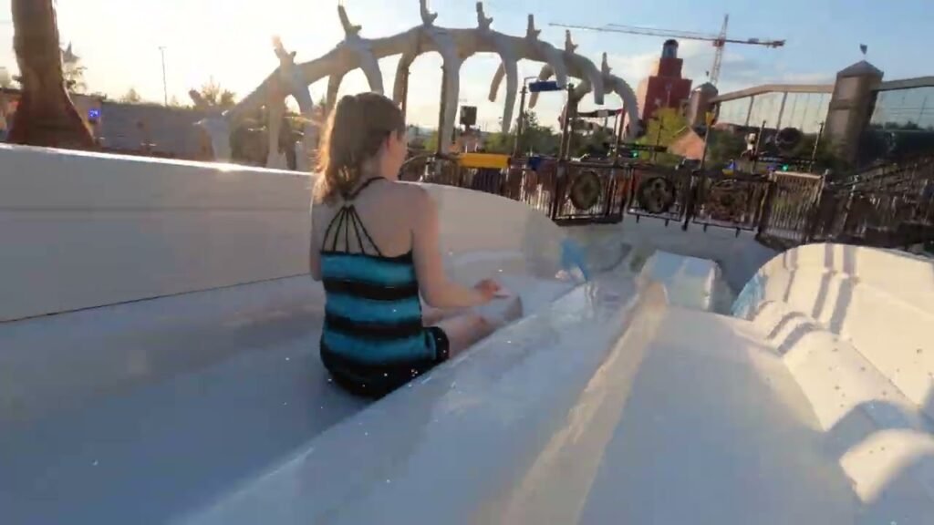 A person sliding down a white water slide on a sunny day at an amusement park. Silver track structure is visible in background.