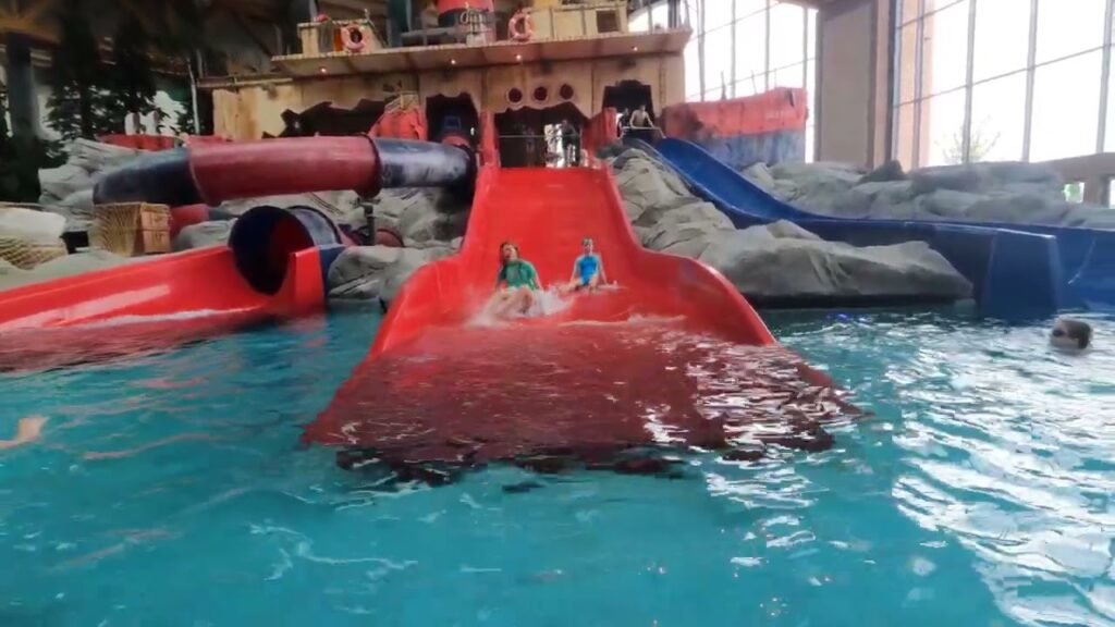 A colorful water slide with red tubes and tunnels is shown in an indoor pool at a water park.