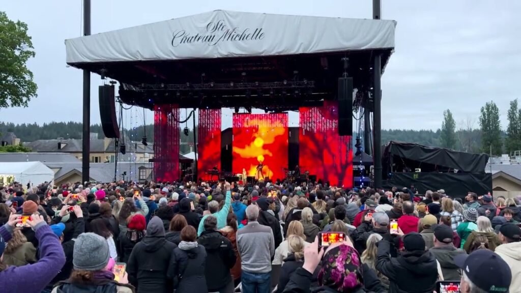 A daytime outdoor music concert at an open-air theater with a stage and banners.
