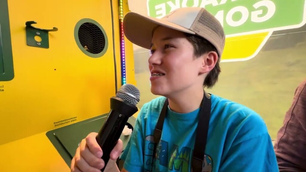 A young person in a teal shirt and cap holding a microphone at a community event.