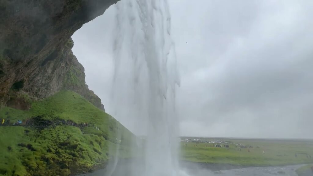 A view of a hidden walkway behind a mossy waterfall, framed by rock and mist.