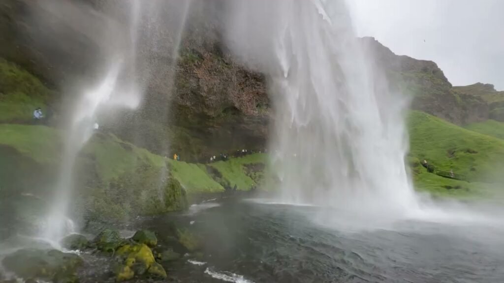 A powerful waterfall cascading over rocky cliffs into a pool, surrounded by vibrant green vegetation and mist, capturing the raw beauty of nature.