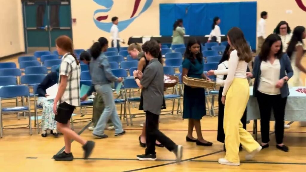 Students walk and chat on a gymnasium floor during a school event.