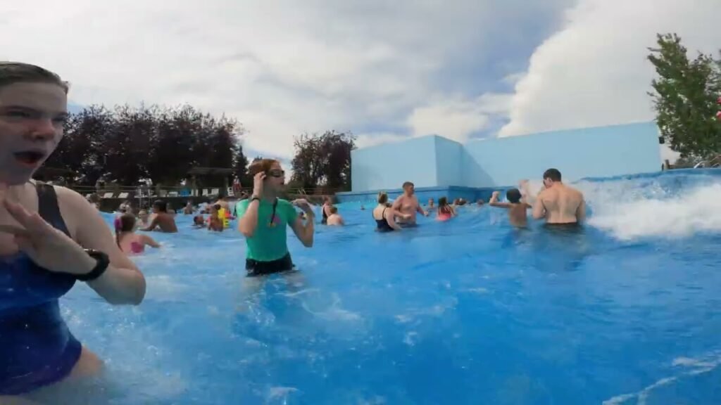 A group of people enjoy a sunny day at an infinity pool. The blue water stretches to the horizon under a partly cloudy sky.