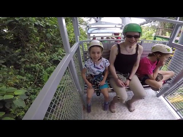 A family enjoys a zipline adventure while wearing helmets and sitting on a metal platform.