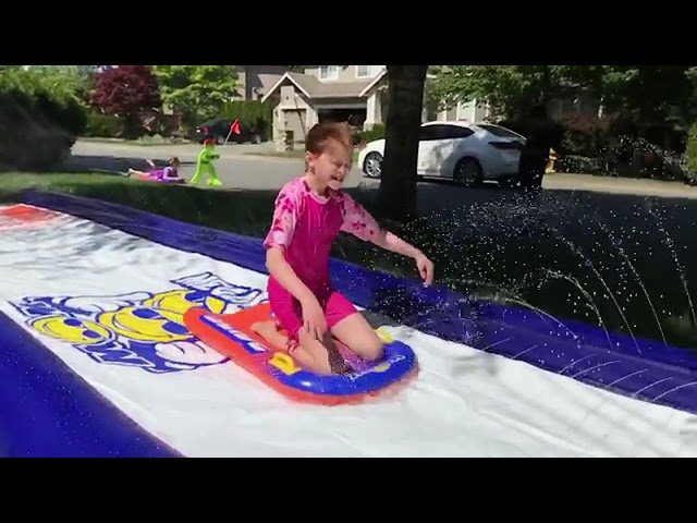 A person in pink swimsuit on a blue and red inflatable slide, sliding down a street during a neighborhood aquatic event.