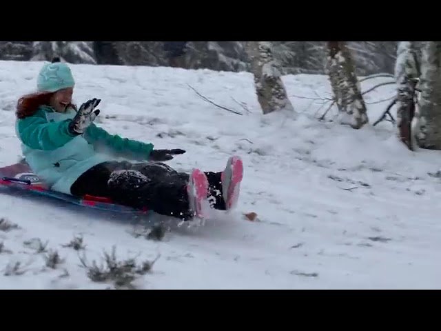 A person clad in a teal jacket and pink slippers sledding down a snowy hill, splashing through the snow with visible movement.