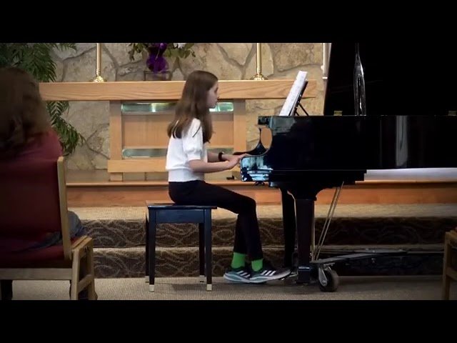 A person seated at a grand piano with a stone wall and wooden screen background.