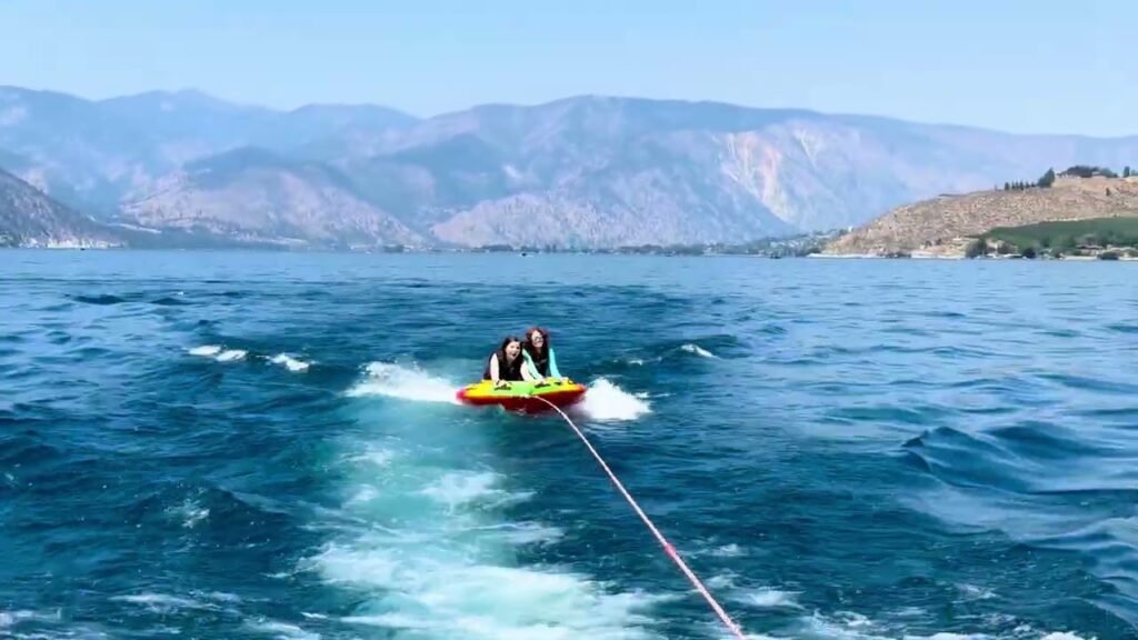 A colorful water tuber being pulled across a pristine blue lake with mountains in the background, capturing an adventurous outdoor moment.