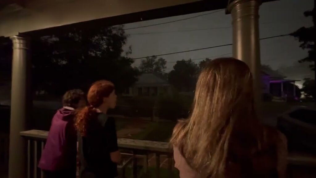 People stand on a porch at twilight, overlooking a tree-lined residential area.