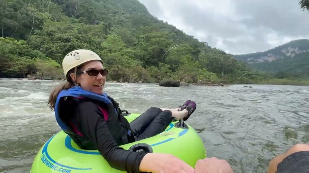 A person in a green river tube glides through a forested waterway in a tropical environment.