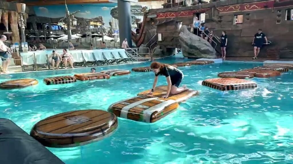 An individual navigates a fun waterpark challenge on floating platforms in a themed pool.