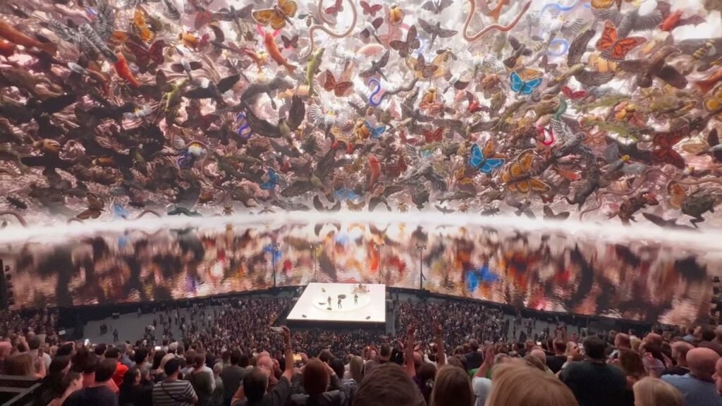 Thousands of live paintings suspended in the air perform at a large venue, with a massive crowd below.