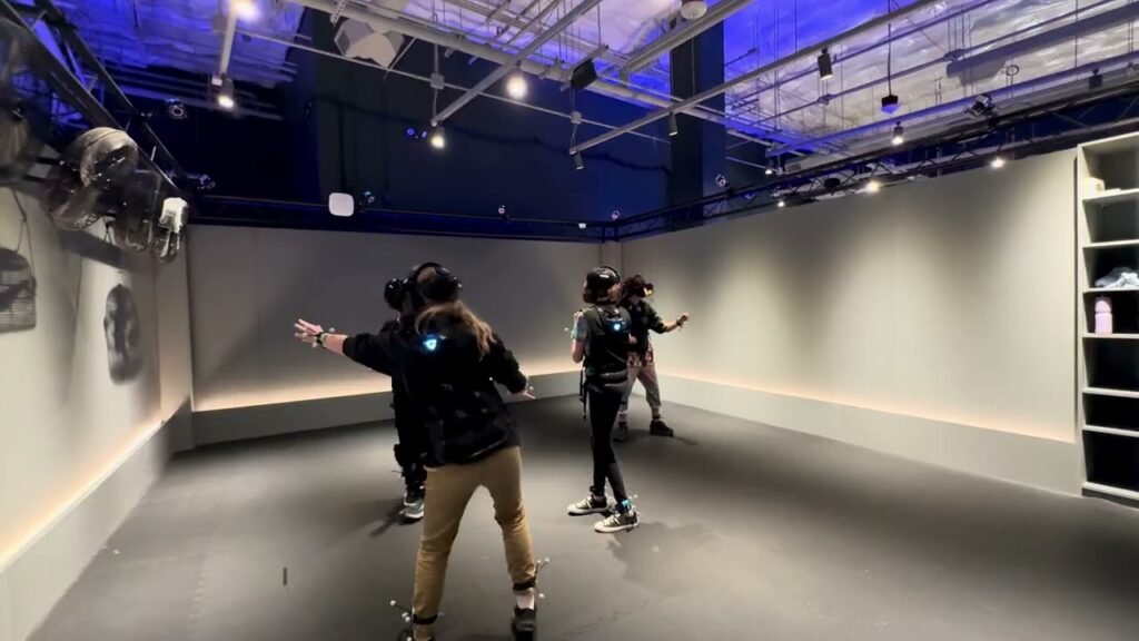 Players engaging in a virtual reality video game session with controllers in a high-tech gaming room. Modern gaming environment with track lighting and various VR interaction features.