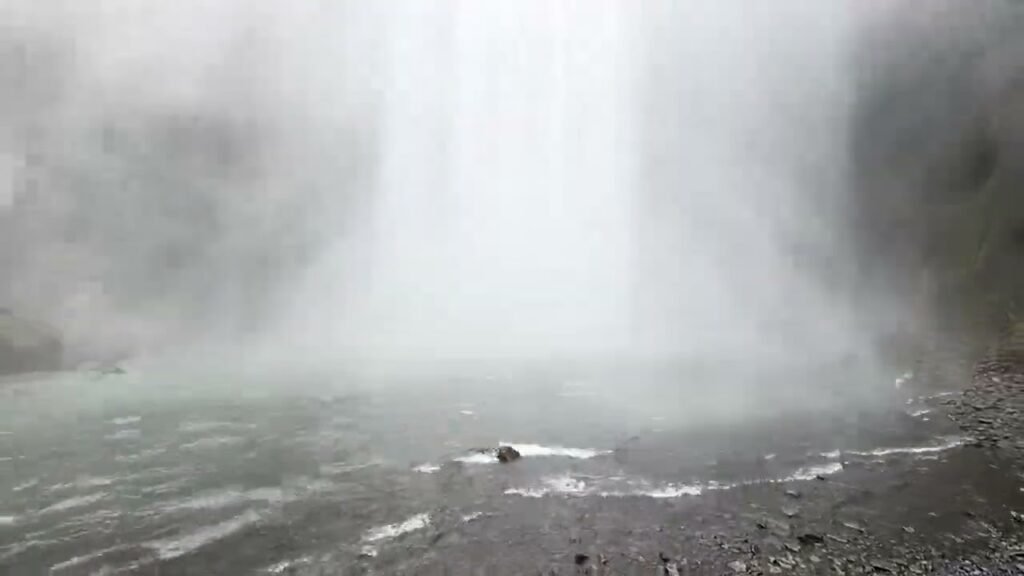 Misty waterfall cascading into a rocky river, creating a foggy atmosphere. This scene is captured in the wild.