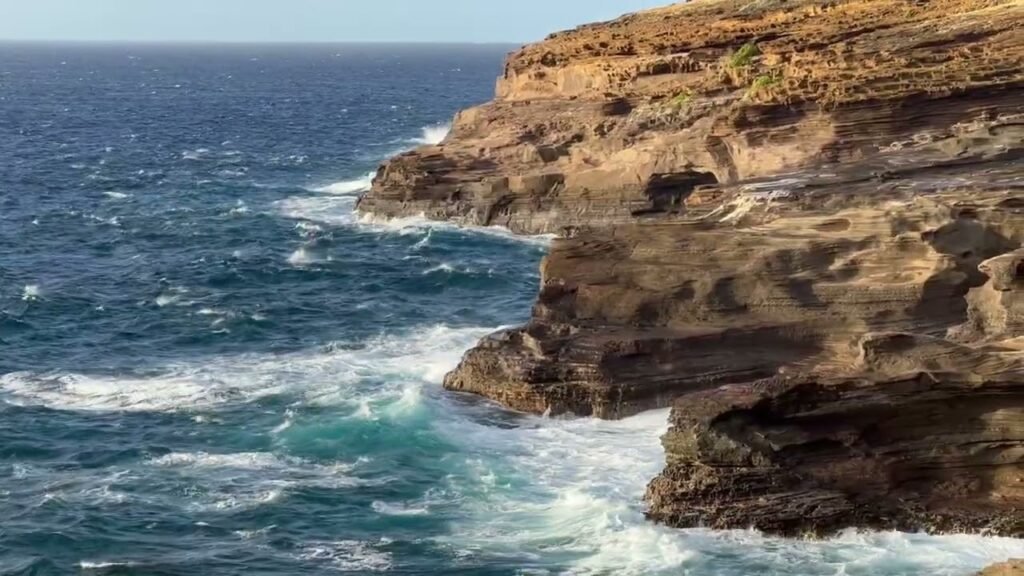 A rugged coastal cliff meeting the deep blue sea with crashing waves at the base.