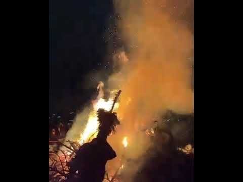 A silhouetted figure stands against a large blaze with orange smoke filling the air.