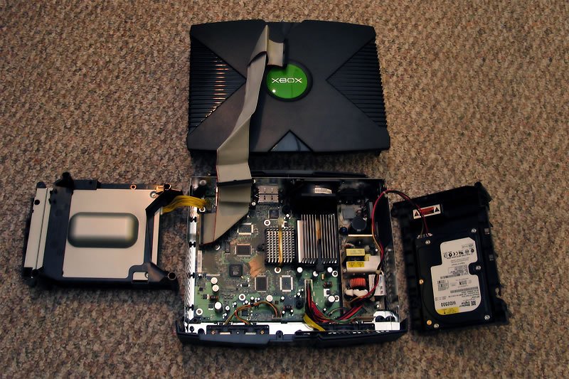 A disassembled Xbox console with internal components laid out on a carpeted surface.
